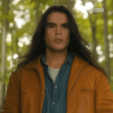 a man with very long hair is wearing a brown leather jacket and a blue shirt .