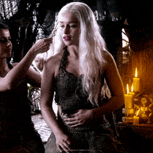 a woman with white hair is being braided by another woman in front of candles