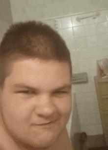 a young man taking a selfie in a bathroom with a tiled wall behind him