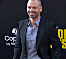 a man in a suit smiles while standing in front of a sign that says co by m