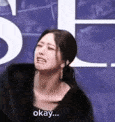 a woman is crying and making a funny face while standing in front of a sign that says okay .