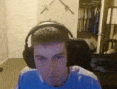 a man wearing headphones looks at the camera in a room with swords on the wall behind him