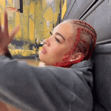 a woman with red braids is leaning against a wall with her arm outstretched