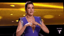 a woman in a blue dress is making a heart shape with her hands .
