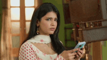 a woman in a white dress is holding a cell phone and looking at it .
