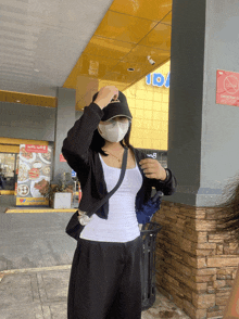 a woman wearing a face mask and a black hat stands in front of a building with a sign that says do not enter