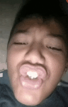 a young boy with a pacifier in his mouth is making a funny face with his eyes closed .