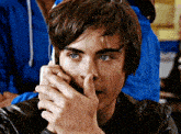 a young man is talking on a cell phone and covering his mouth with his hand