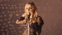 a woman singing into a microphone with her hand on her face