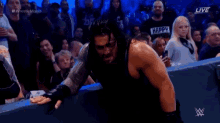 roman reigns is standing in front of a crowd while wearing a black armor .