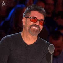 a man wearing red glasses is smiling in front of a microphone with a star on it
