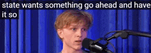 a young man is standing in front of a microphone with the words state wants something go ahead and have it so above him .