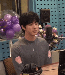 a man wearing headphones is sitting in front of a microphone with purple balloons behind him
