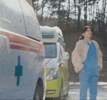 a woman in scrubs stands in front of a row of ambulance vans