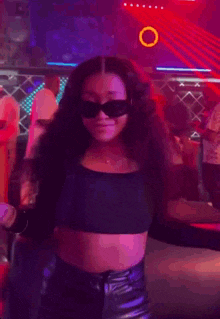 a woman wearing sunglasses and a crop top is dancing in a nightclub .