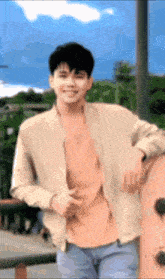 a young man in a tan jacket and orange shirt is leaning against a wall .