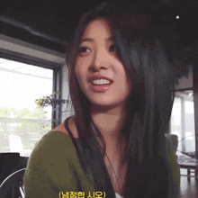 a woman in a green sweater is smiling in front of a window with chinese writing on it