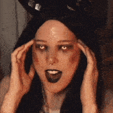 a woman in a devil costume with horns on her head is holding her hands to her head .