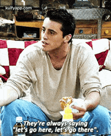 a man is sitting on a couch eating a hot dog and holding a bottle of mustard .