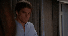 a man in a blue shirt is standing next to a window in a dark room .