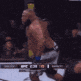 a man without a shirt is standing in a boxing ring with a crowd watching .