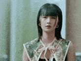 a woman wearing a floral collar and hoop earrings looks at the camera