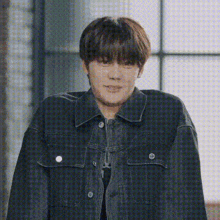 a young man wearing a black denim jacket is smiling and looking at the camera .