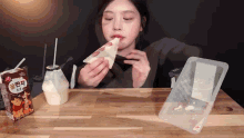 a woman is sitting at a table eating a sandwich next to a carton of winnie the pooh milk