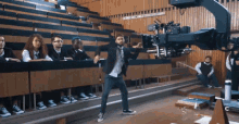 a man in a suit and tie is dancing in front of a camera in a lecture hall