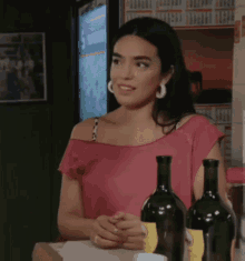 a woman in a pink off the shoulder top is sitting at a bar holding a bottle of wine