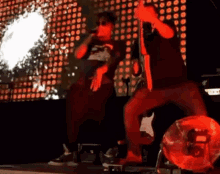 a man is singing into a microphone on a stage while another man is kneeling down .