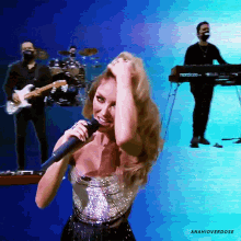 a woman singing into a microphone in front of a keyboard and a man playing drums