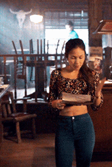 a woman in a floral top and blue jeans is standing in a bar