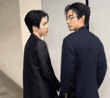 two men in suits and glasses are standing next to each other holding hands .
