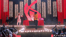 a man stands on a stage in front of a crowd with a large k on the background