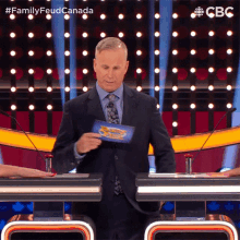 a man in a suit and tie is holding a piece of paper that says family feud canada on it