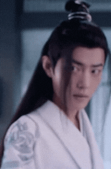 a man with long hair is wearing a white robe and has a ponytail .