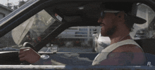 a man wearing sunglasses and a hat is driving a car with the letter r on the side