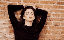 a woman is standing in front of a brick wall with her eyes closed