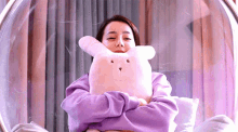 a woman in a purple sweatshirt is holding a pink stuffed rabbit .