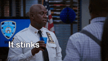 a man in a police uniform is holding a blue cup and says it stinks