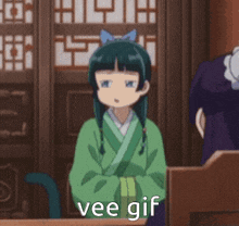a girl in a green kimono is sitting at a table with the words vee gif written on it .