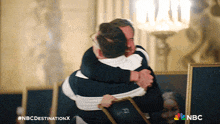 two men hugging with nbc destination x written on the bottom right