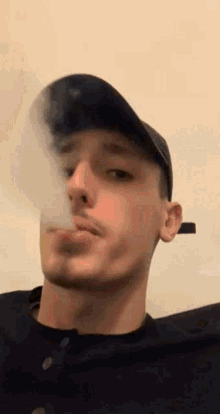 a man wearing a hat is smoking a cigarette and blowing smoke out of his mouth .
