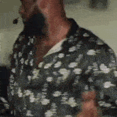 a man wearing a floral shirt and a microphone is talking on a cell phone .
