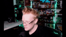 a man wearing glasses and a black shirt is sitting in front of a microphone in a room filled with toys