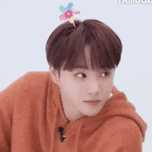 a young man with a flower in his hair is wearing an orange sweater and a microphone .