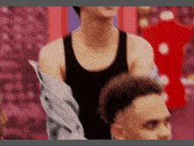 a man in a black tank top and a denim jacket is standing next to another man