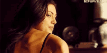 a woman in a black bra is looking over her shoulder at the camera in a dark room .
