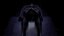 a man in a black suit is sitting in a chair in the dark .